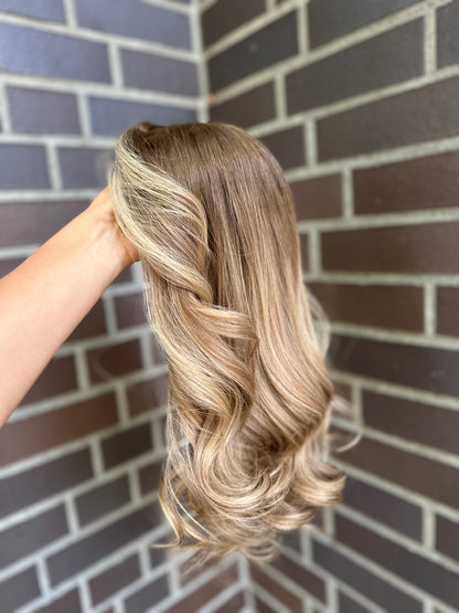 Bild zeigt blondes Echthaarteil, das seitlich ins Bild gehalten wird. Bild dient der Produktpräsentation eines Artikels in der Kategorie Topper/Perücken.
