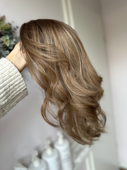 Bild zeigt blondes Echthaarteil, das seitlich ins Bild gehalten wird. Bild dient der Produktpräsentation eines Artikels in der Kategorie Topper/Perücken.