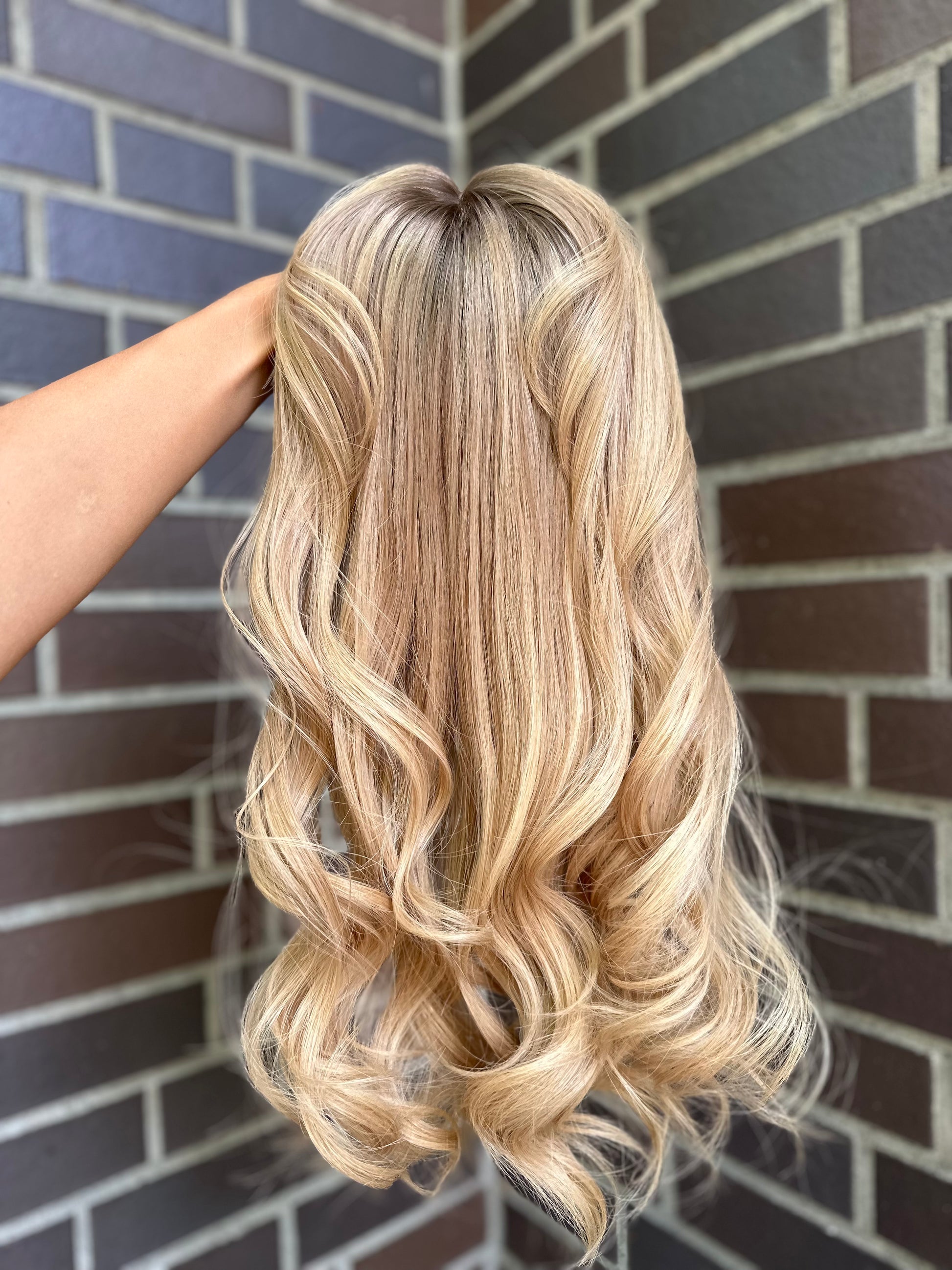 Bild zeigt blondes Echthaarteil, das frontal ins Bild gehalten wird. Bild dient der Produktpräsentation eines Artikels in der Kategorie Topper/Perücken.