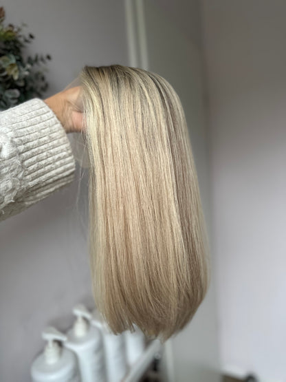 Bild zeigt blondes Echthaarteil, das seitlich ins Bild gehalten wird. Bild dient der Produktpräsentation eines Artikels in der Kategorie Topper/Perücken.