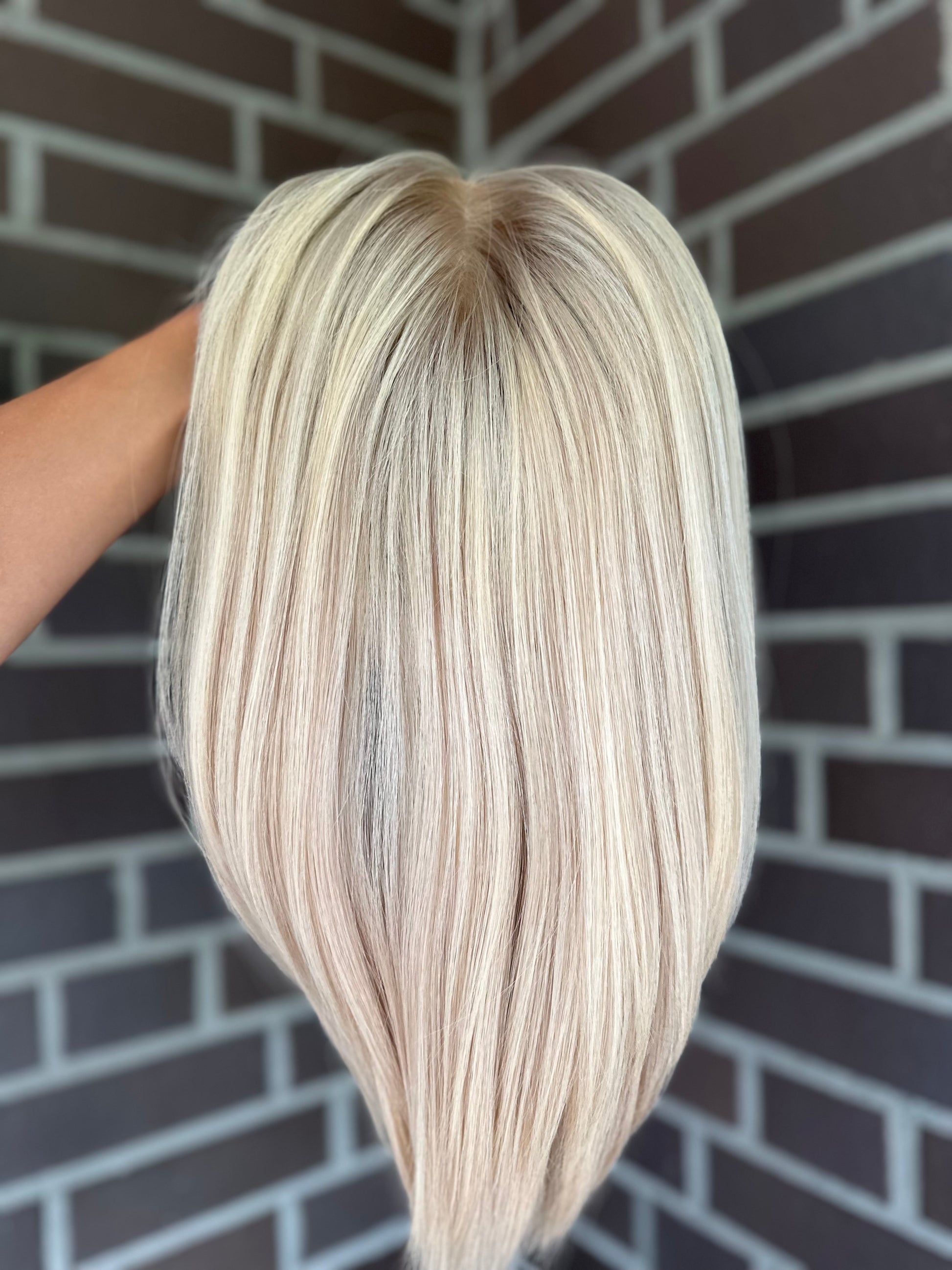 Bild zeigt blondes Echthaarteil, das frontal ins Bild gehalten wird. Bild dient der Produktpräsentation eines Artikels in der Kategorie Topper/Perücken.