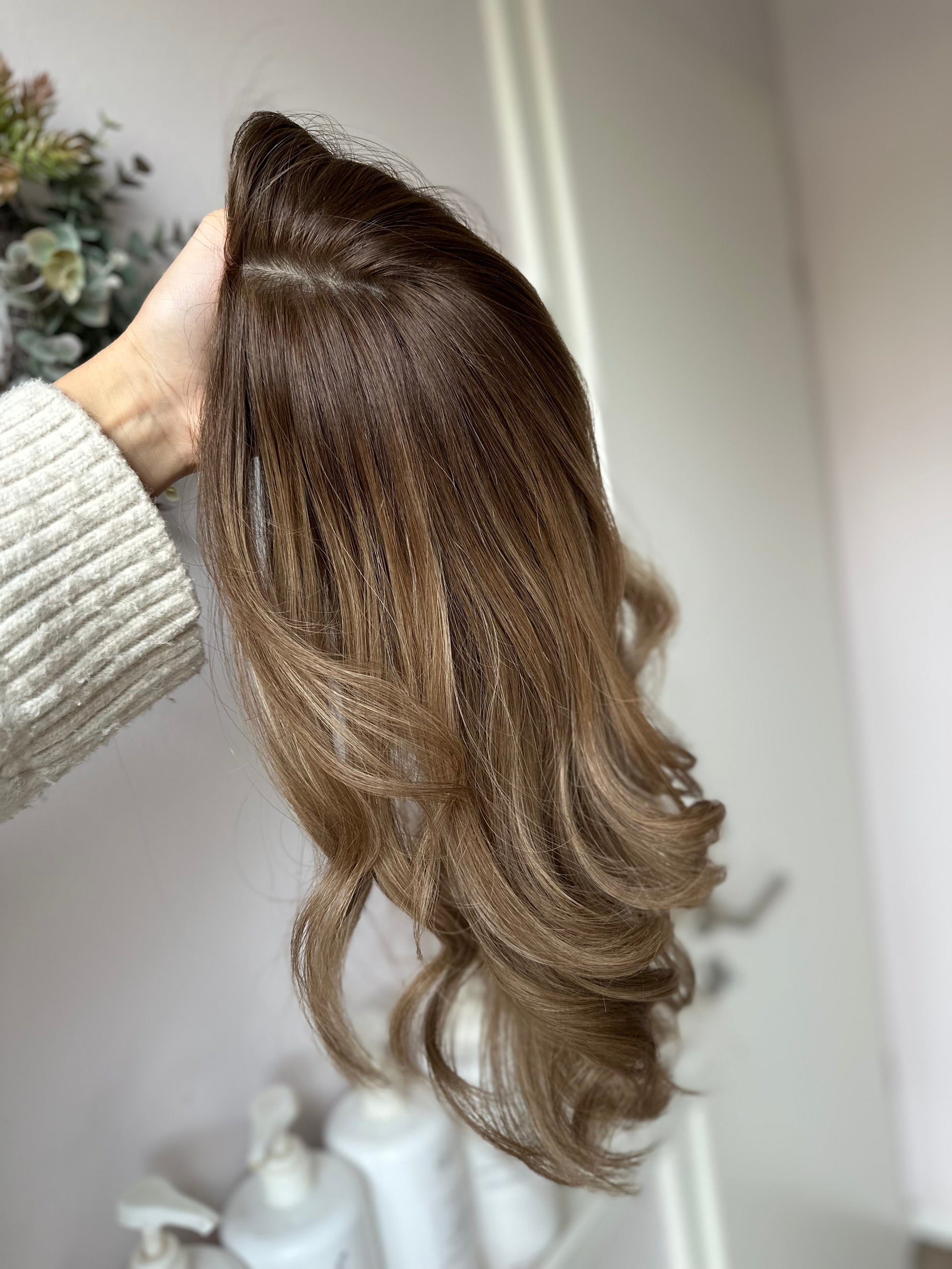 Bild zeigt blondes Echthaarteil, das seitlich ins Bild gehalten wird. Bild dient der Produktpräsentation eines Artikels in der Kategorie Topper/Perücken.