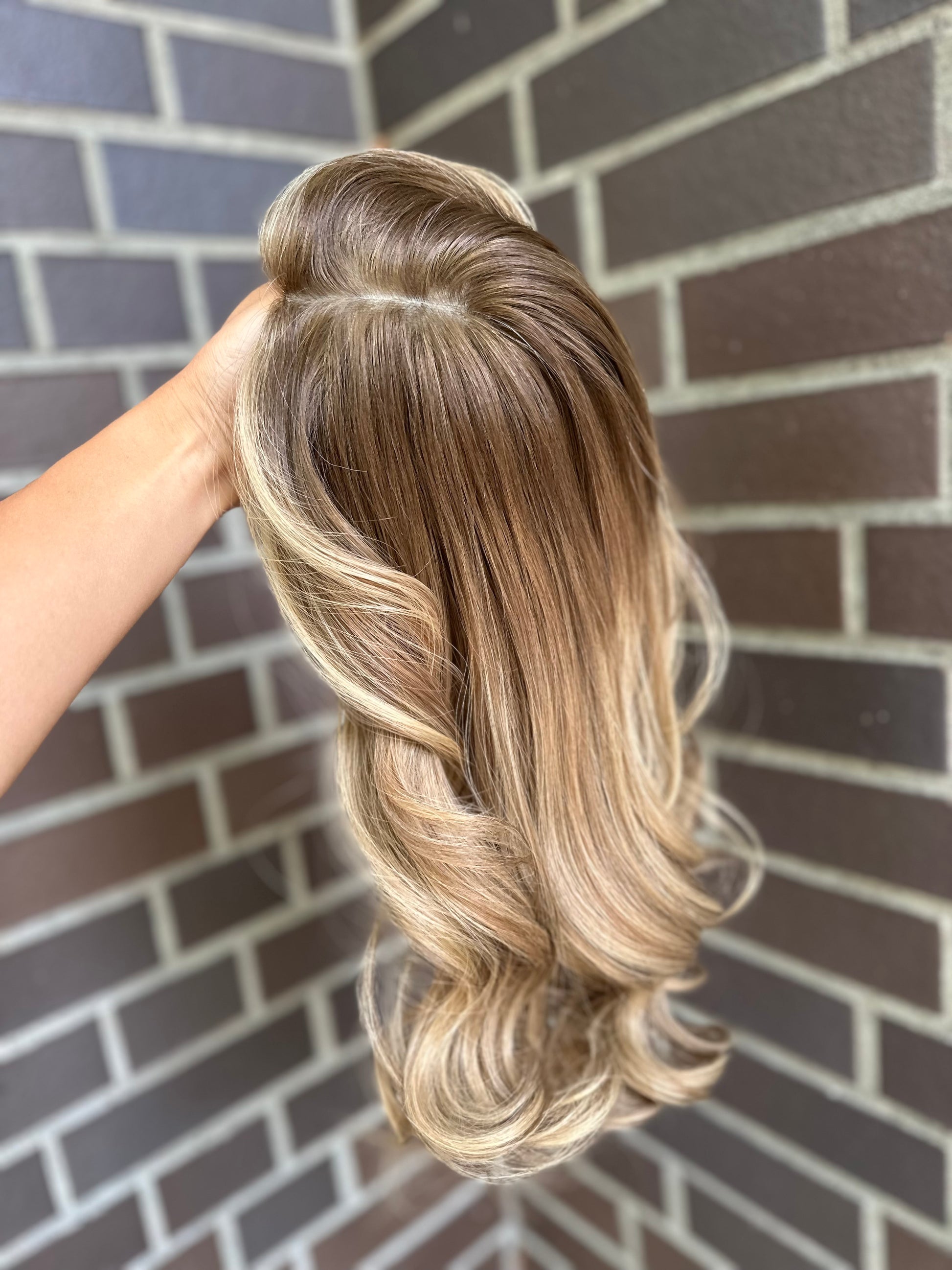 Bild zeigt blondes Echthaarteil, das seitlich ins Bild gehalten wird. Bild dient der Produktpräsentation eines Artikels in der Kategorie Topper/Perücken.