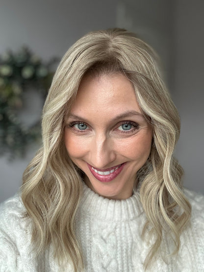 Bild zeigt blondes Echthaarteil, das frontal ins Bild gehalten wird. Bild dient der Produktpräsentation eines Artikels in der Kategorie Topper/Perücken.