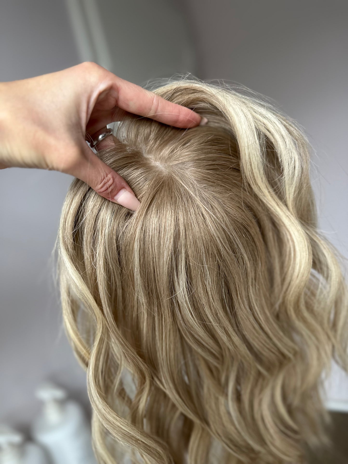 Bild zeigt blondes Echthaarteil, das frontal ins Bild gehalten wird. Bild dient der Produktpräsentation eines Artikels in der Kategorie Topper/Perücken.