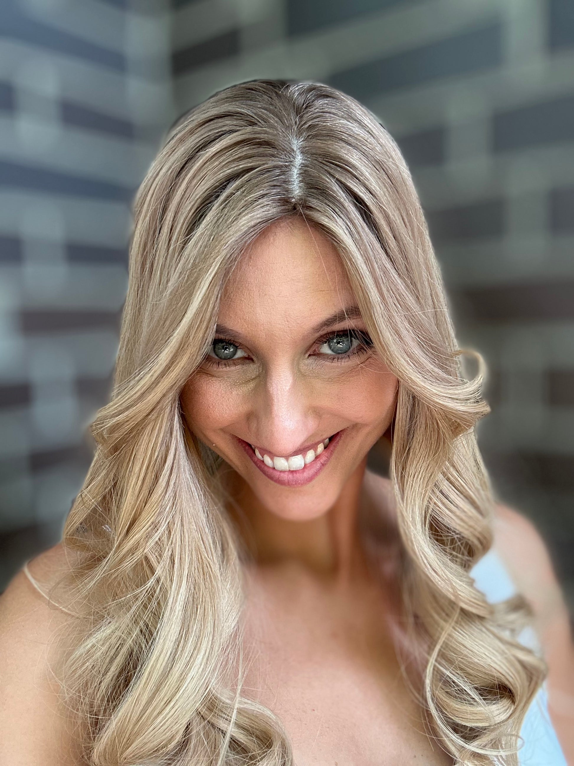 Bild zeigt attraktive Frau, die ihren Kopf leicht beugt, sodass blonder Haaransatz sichtbar wird. Bild dient der Produktpräsentation eines Artikels in der Kategorie Topper/Perücken.