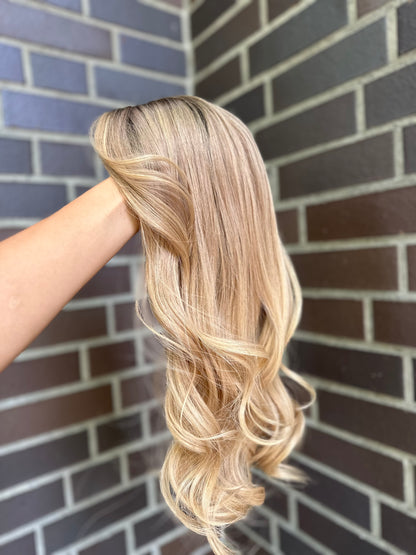 Bild zeigt blondes Echthaarteil, das seitlich ins Bild gehalten wird. Bild dient der Produktpräsentation eines Artikels in der Kategorie Topper/Perücken.