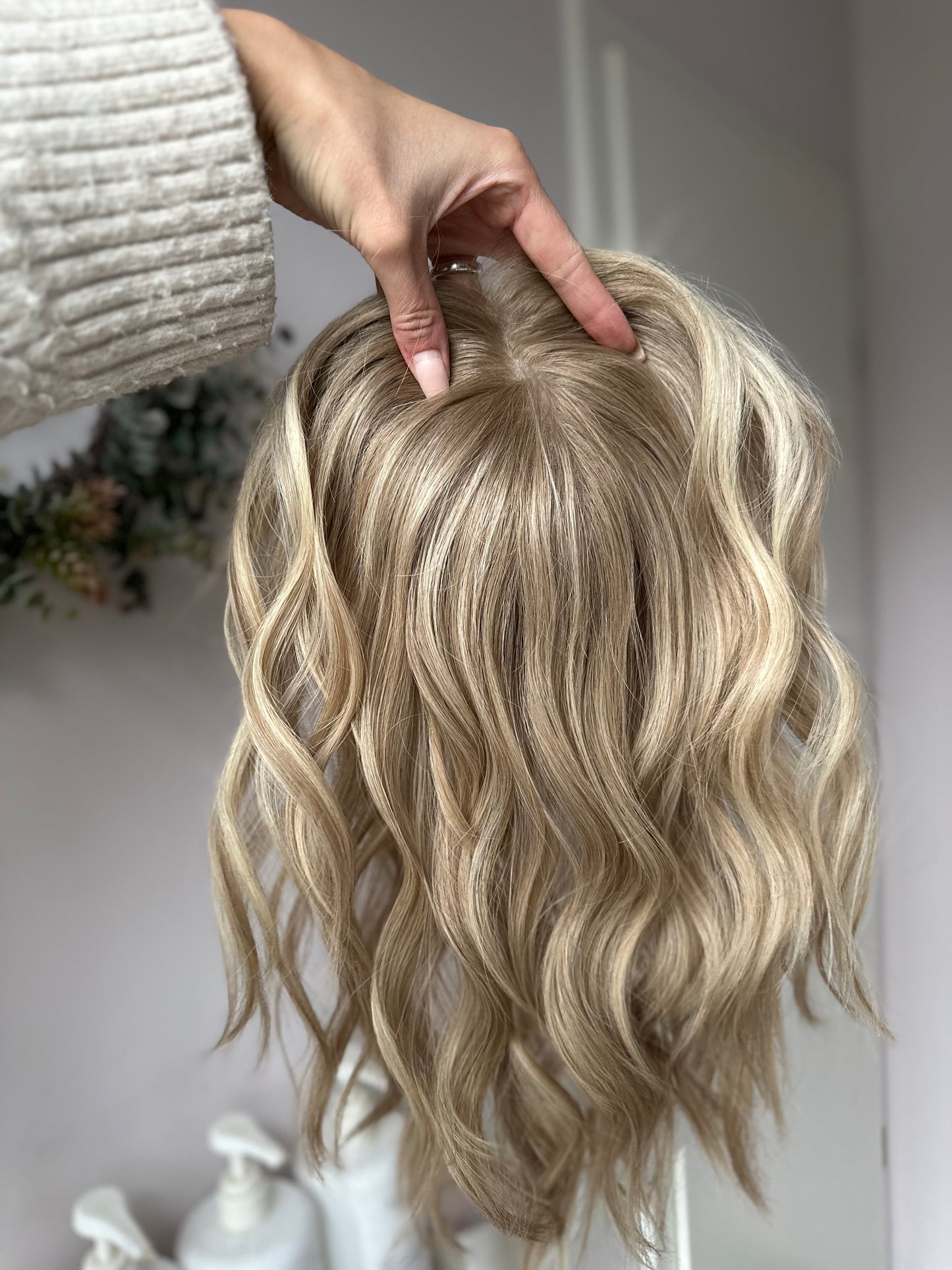 Bild zeigt blondes Echthaarteil, das frontal ins Bild gehalten wird. Bild dient der Produktpräsentation eines Artikels in der Kategorie Topper/Perücken.