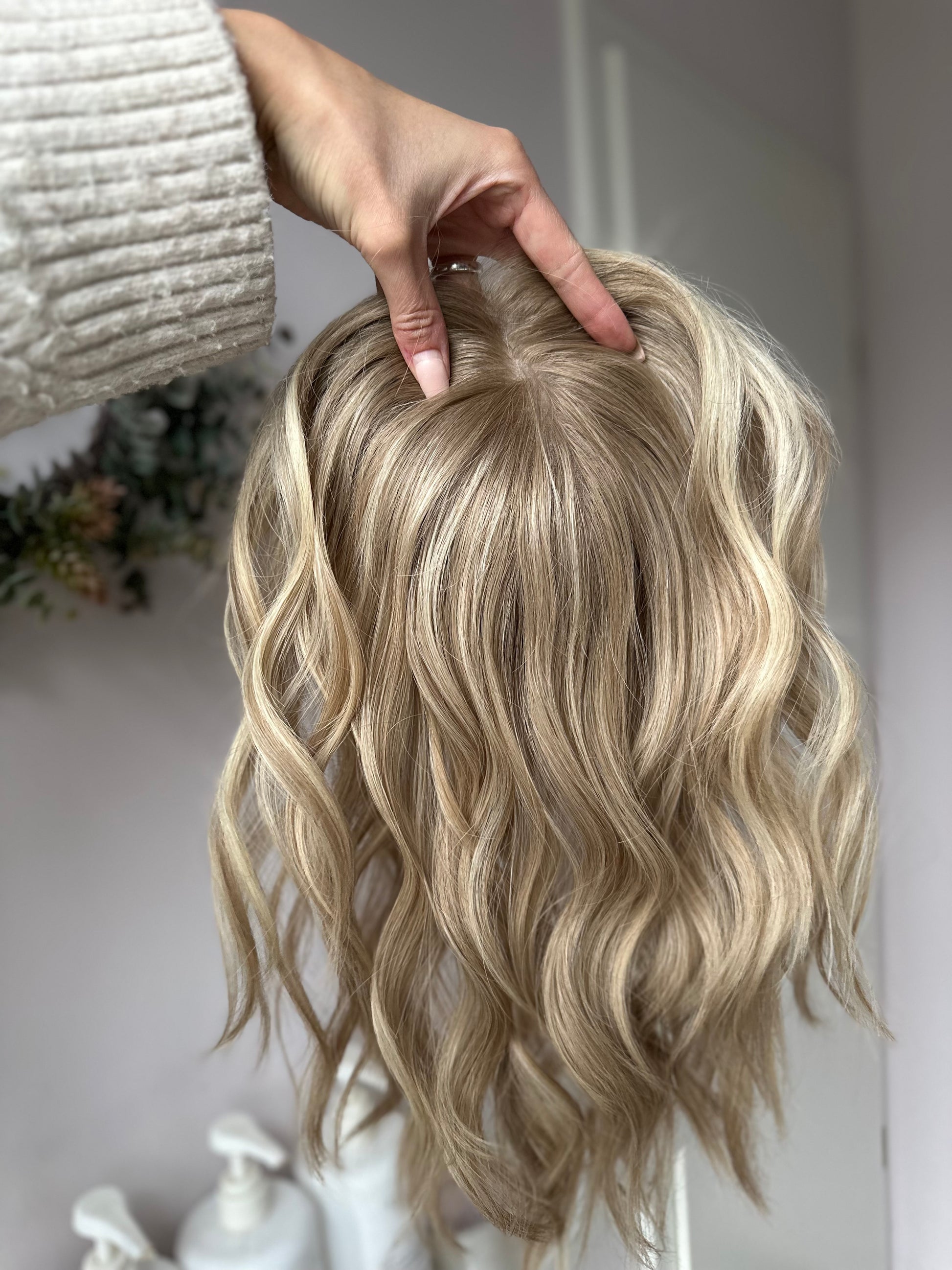 Bild zeigt blondes Echthaarteil, das frontal ins Bild gehalten wird. Bild dient der Produktpräsentation eines Artikels in der Kategorie Topper/Perücken.