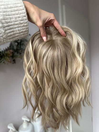 Bild zeigt blondes Echthaarteil, das frontal ins Bild gehalten wird. Bild dient der Produktpräsentation eines Artikels in der Kategorie Topper/Perücken.