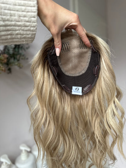 Bild zeigt blondes Echthaarteil, das frontal ins Bild gehalten wird. Bild dient der Produktpräsentation eines Artikels in der Kategorie Topper/Perücken.