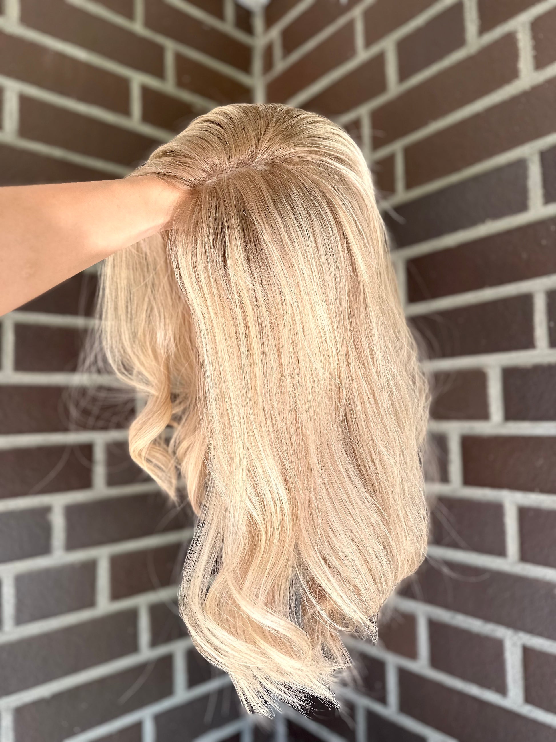 Bild zeigt blondes Echthaarteil, das seitlich ins Bild gehalten wird. Bild dient der Produktpräsentation eines Artikels in der Kategorie Topper/Perücken.