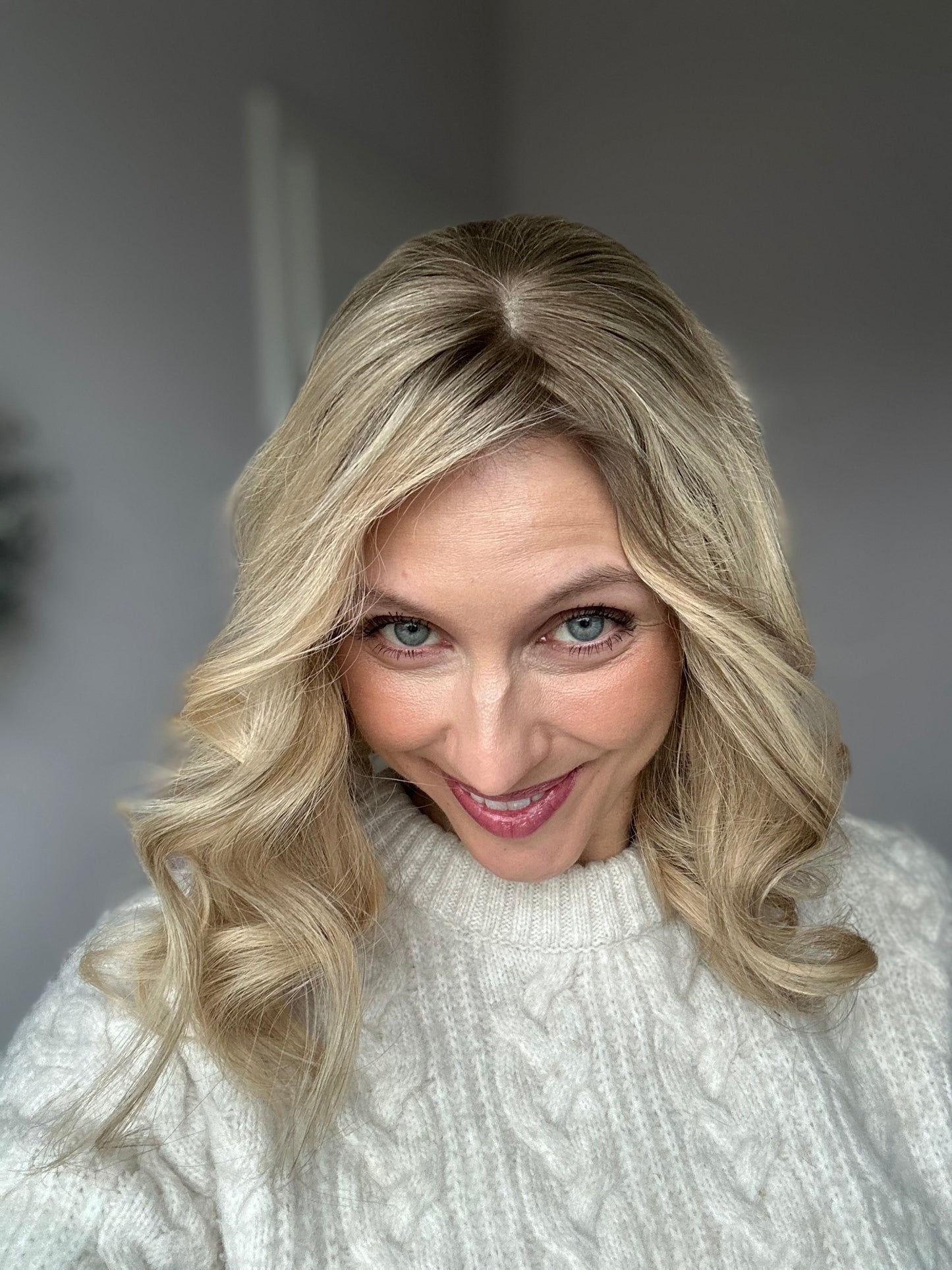 Bild zeigt blondes Echthaarteil, dessen Haaransatz  ins Bild gehalten wird. Bild dient der Produktpräsentation in der Kategorie Topper/Perücken.