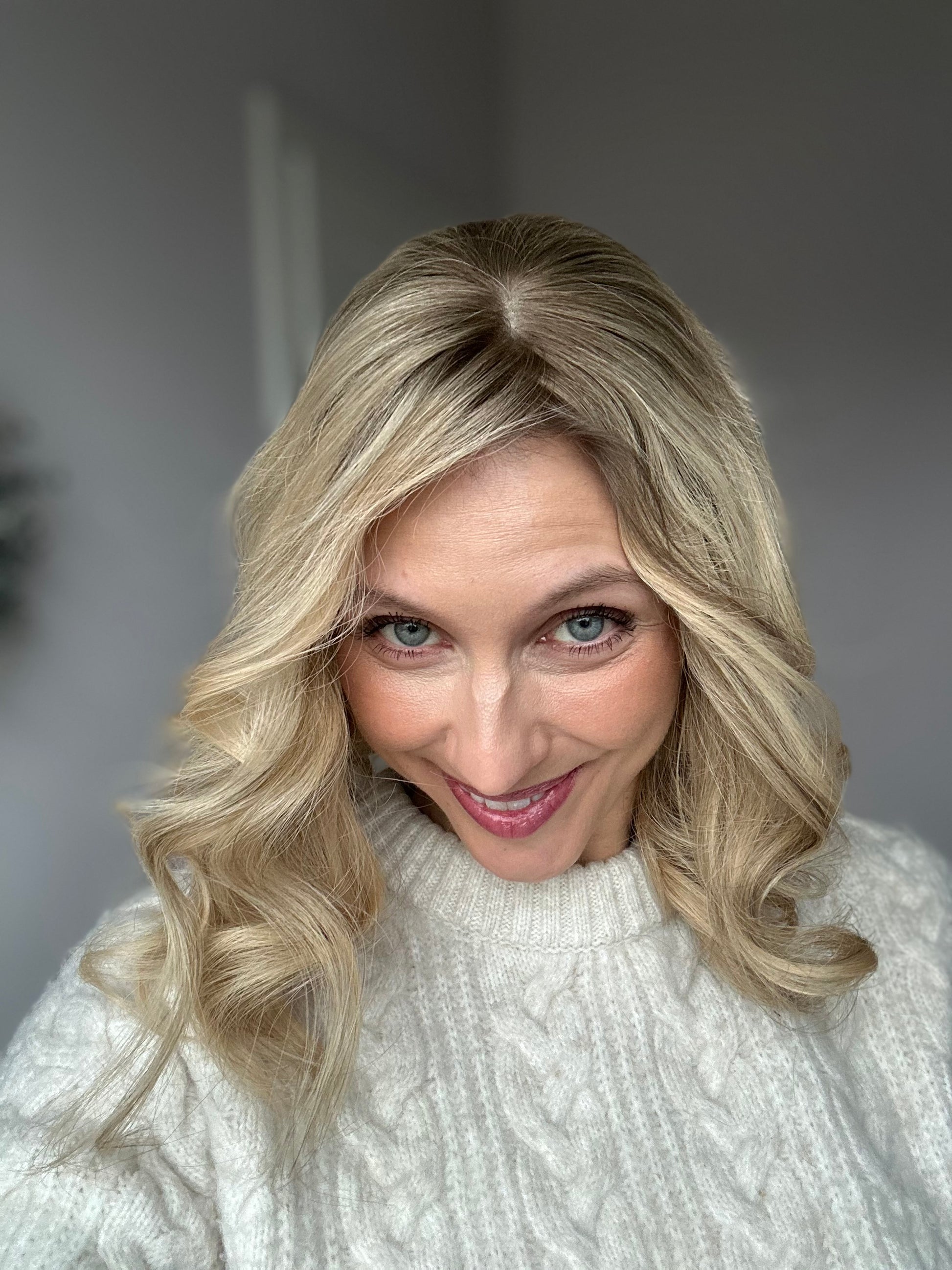 Bild zeigt blondes Echthaarteil, dessen Haaransatz  ins Bild gehalten wird. Bild dient der Produktpräsentation in der Kategorie Topper/Perücken.