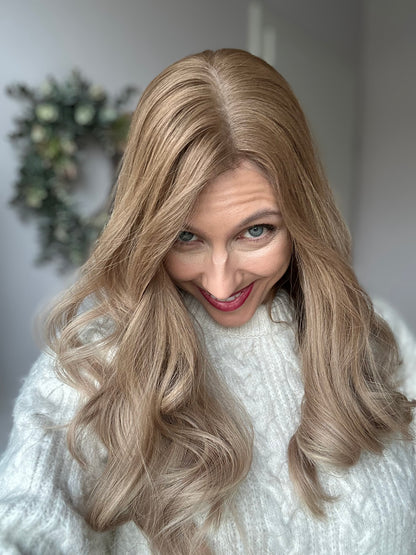 Bild zeigt attraktive Frau, die ihren Kopf leicht beugt, sodass blonder Haaransatz sichtbar wird. Bild dient der Produktpräsentation eines Artikels in der Kategorie Topper/Perücken.