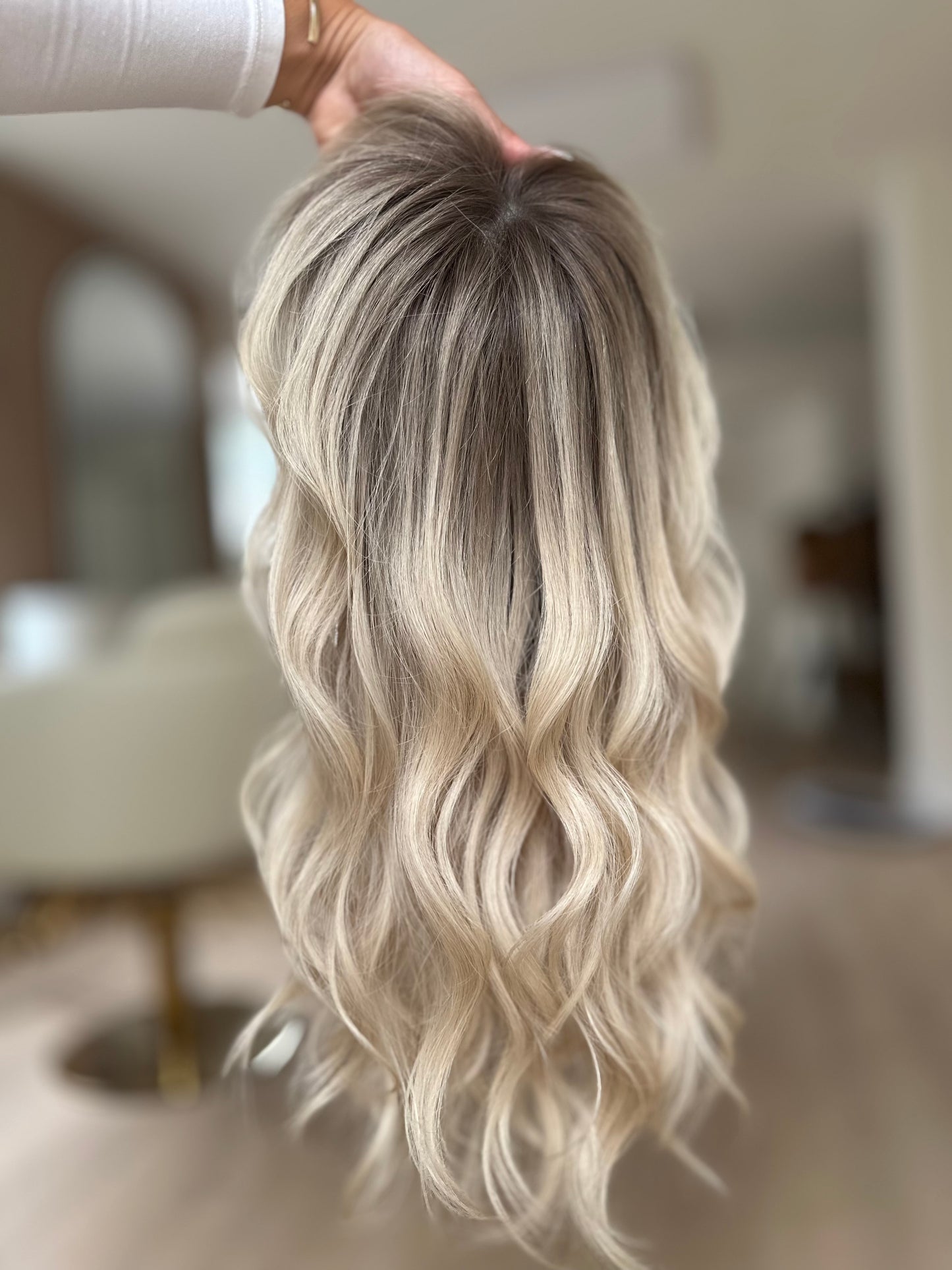 Bild zeigt blondes Echthaarteil, das frontal ins Bild gehalten wird. Bild dient der Produktpräsentation eines Artikels in der Kategorie Topper/Perücken.